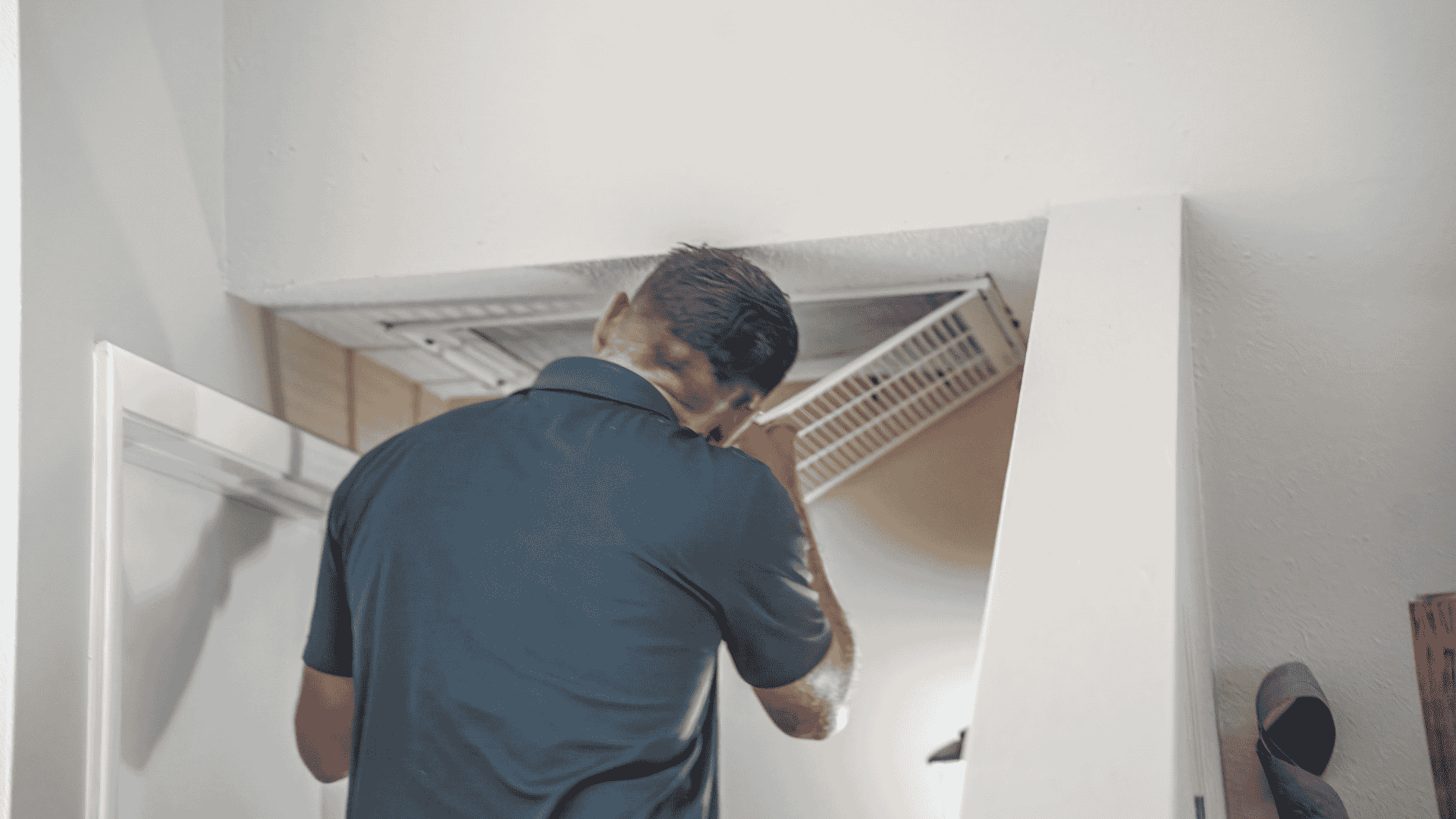 Air Titans specialist reaching into an open ceiling duct with a brush attachment, vacuuming dust and debris from inside the air duct.