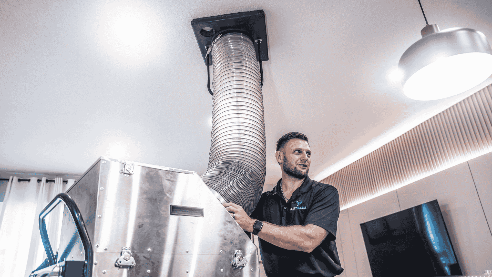 Technician positions a large vacuum hose into a ceiling duct connection, sealing and testing for air leaks in the home’s duct system.