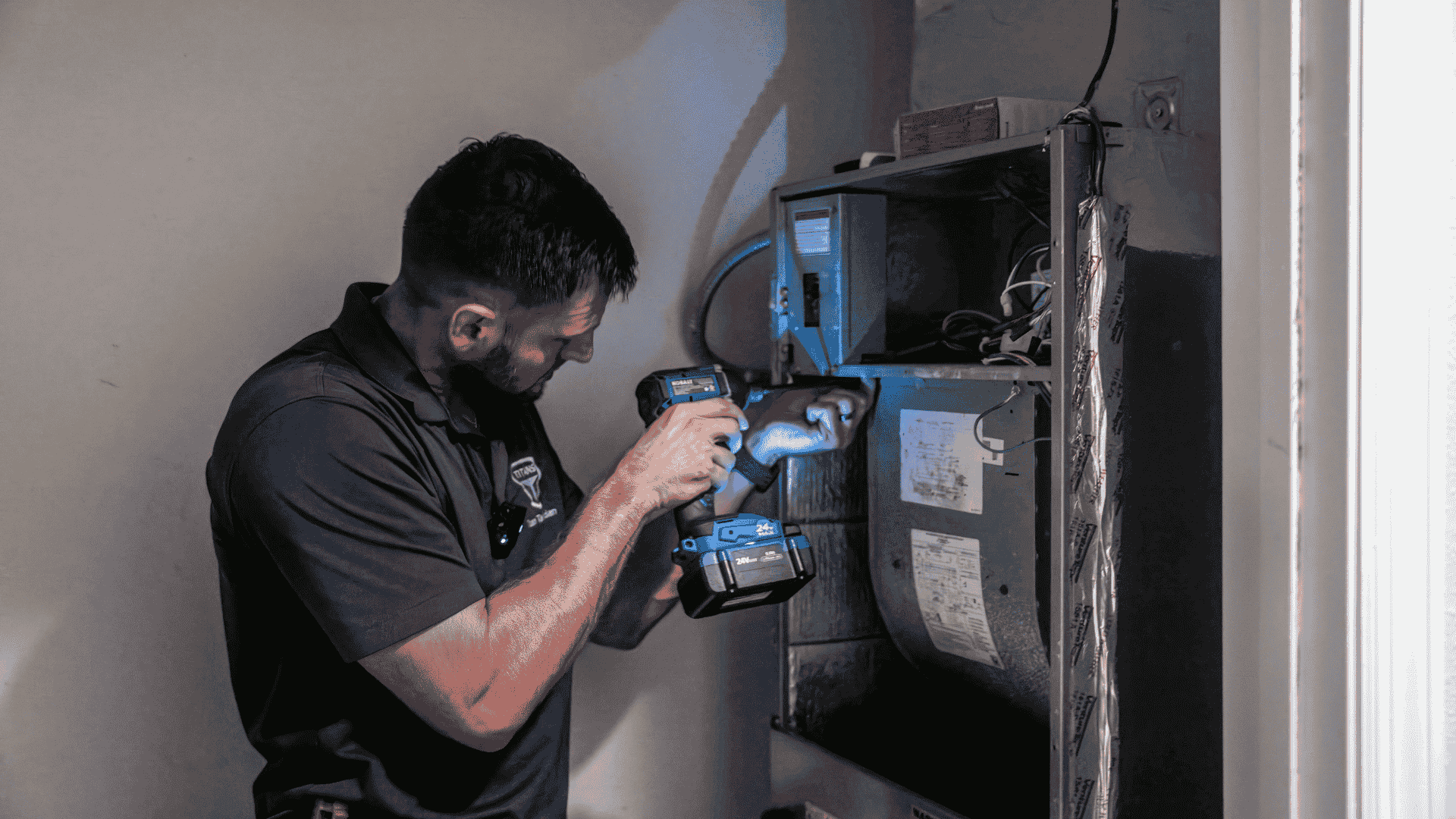 An Air Titans installer carries a large blower wheel out of an HVAC cabinet during a system installation.