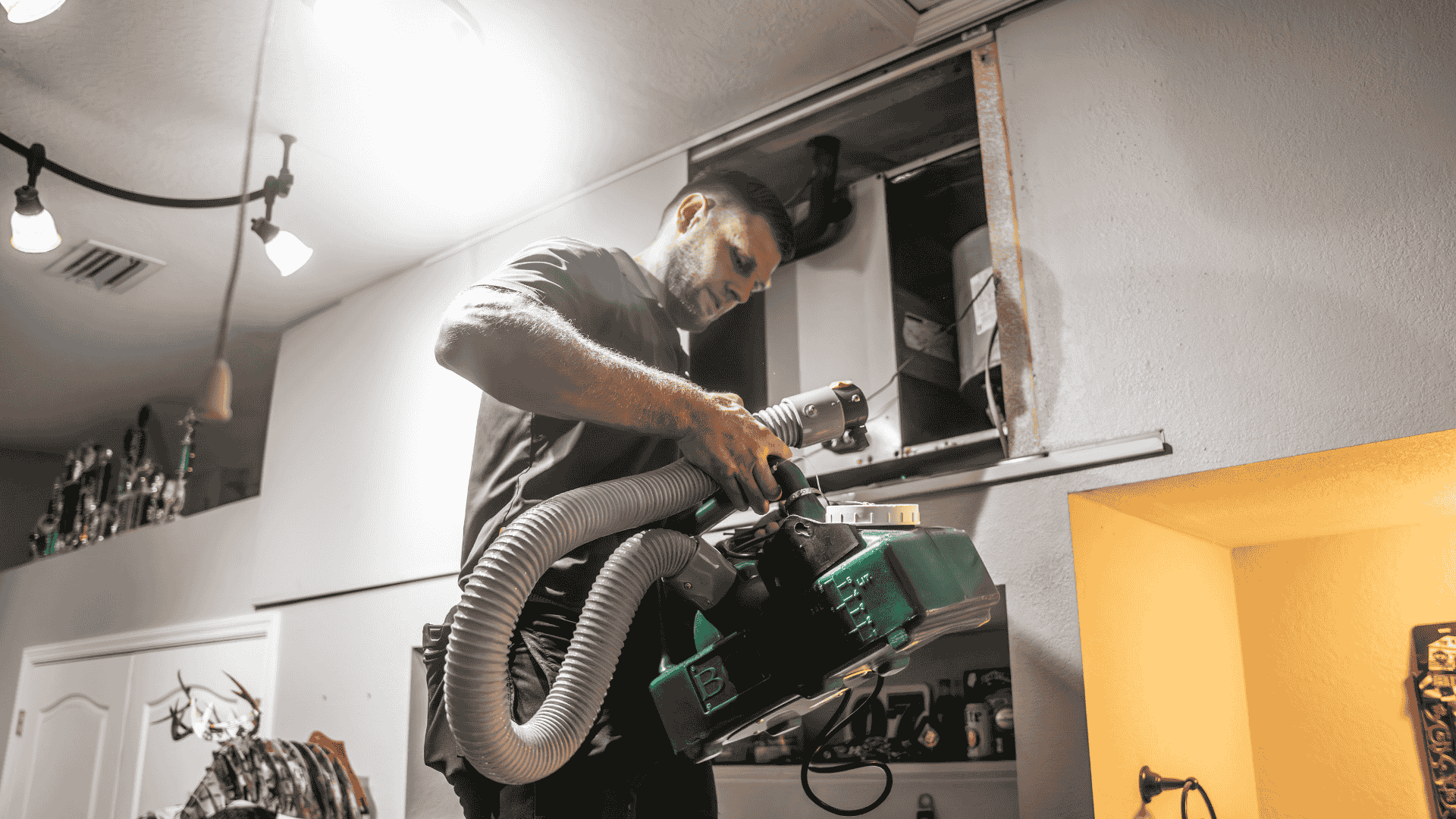 A technician vacuum-cleans inside an air duct with a flexible hose attachment as part of routine HVAC maintenance.