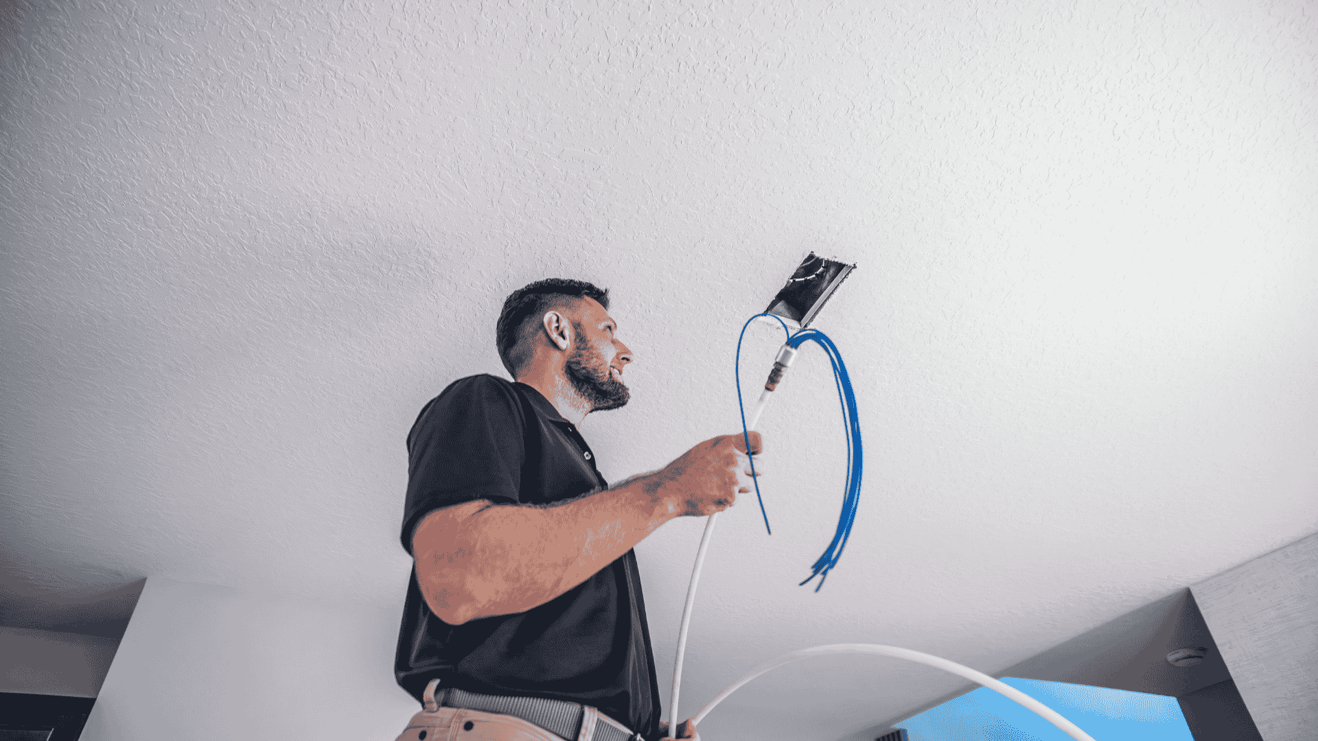 Air Titans technician standing on a ladder, holding a UV lamp assembly and electrical wiring as he installs a ceiling-mounted UV air sanitizer into the home’s HVAC duct.